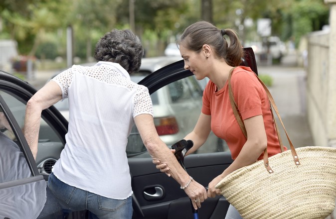 Un aidant aide une dame à monter dans la voiture